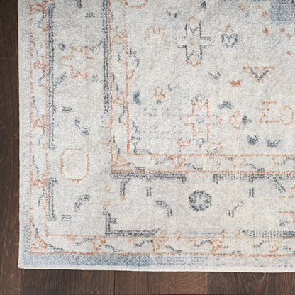 Woven light gray area rug with blue and orange geometric border and pattern, laid on dark wood floor.