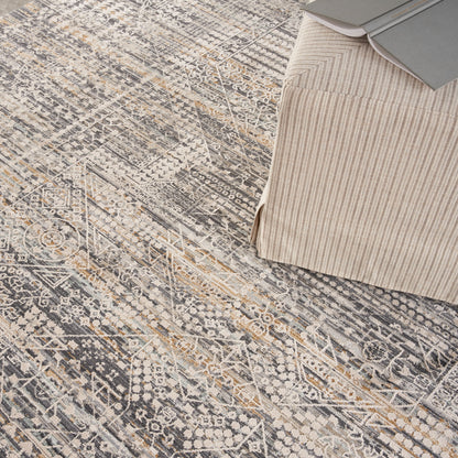 Neutral area rug with distressed geometric pattern in gray, ivory and gold accents; beige striped ottoman with magazines.