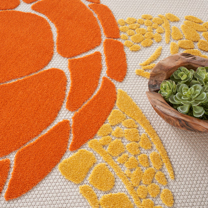Orange & yellow geometric tufted rug with a wooden bowl of succulents on a textured floor.