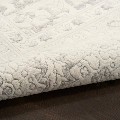 Cream textured rug with subtle floral and geometric border, plush pile on dark wood floor.