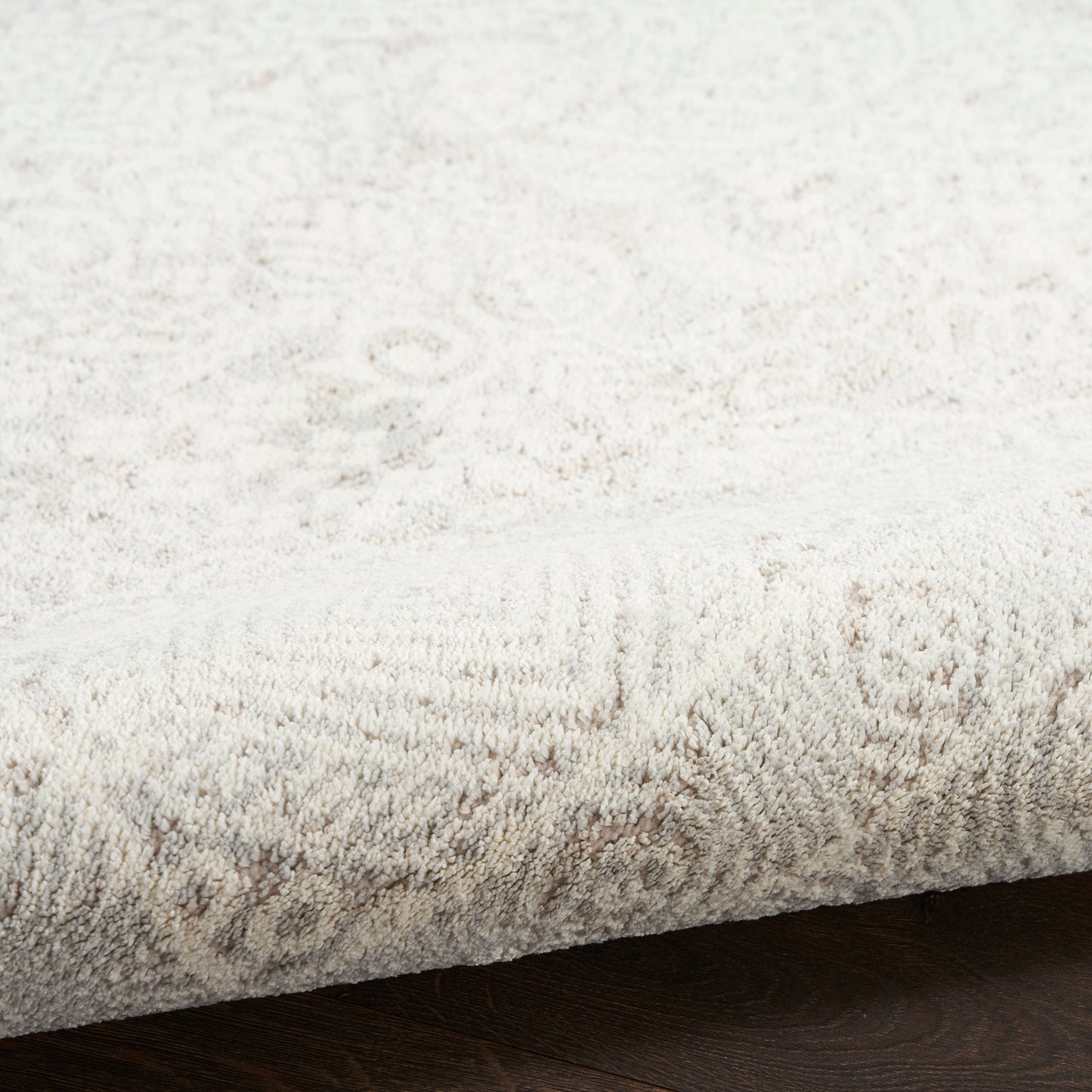 Cream plush rug with subtle distressed pattern, rolled edge, resting on dark wooden floor.