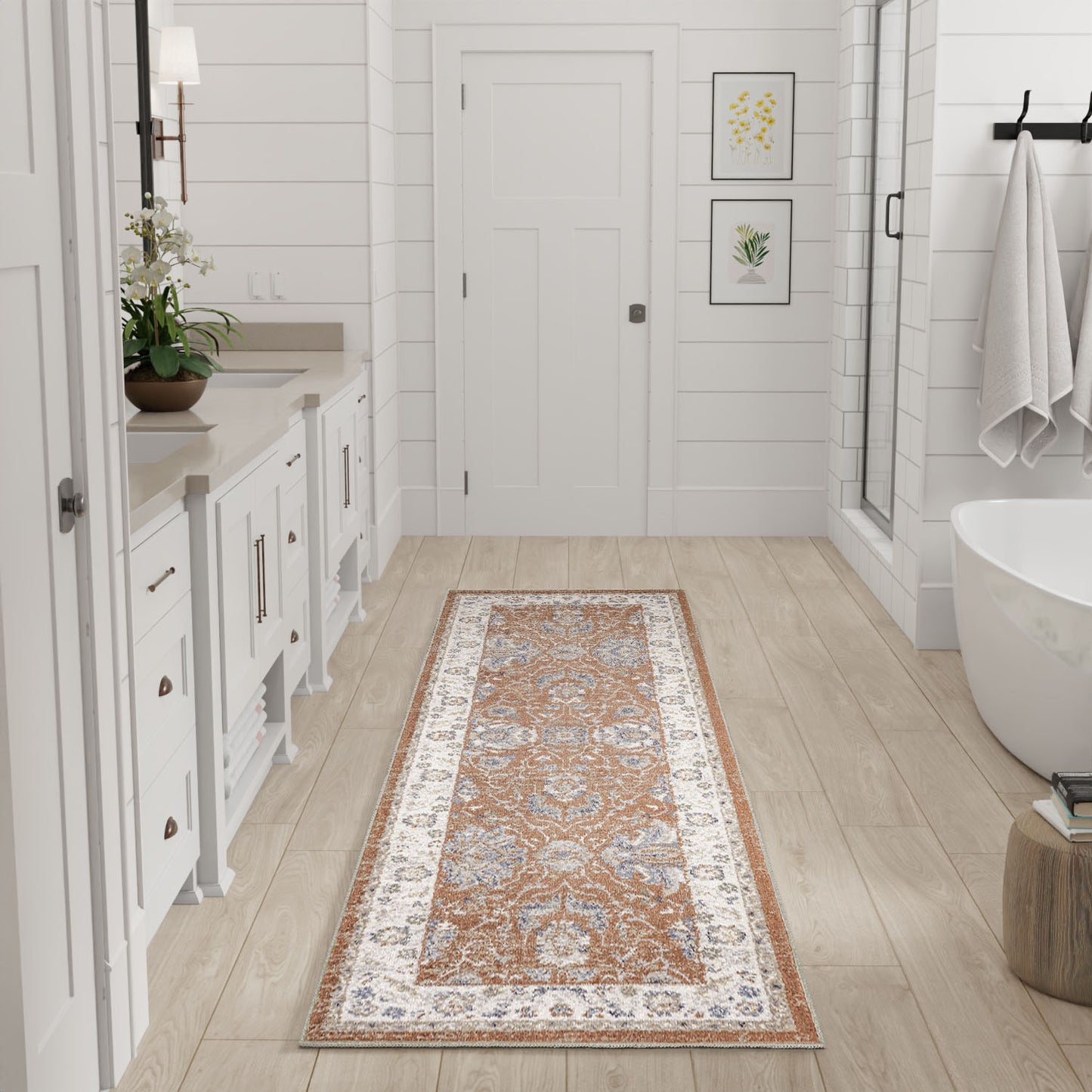 Persian-inspired runner rug in orange, ivory & blue on light wood floor in a white bathroom with vanity and freestanding tub