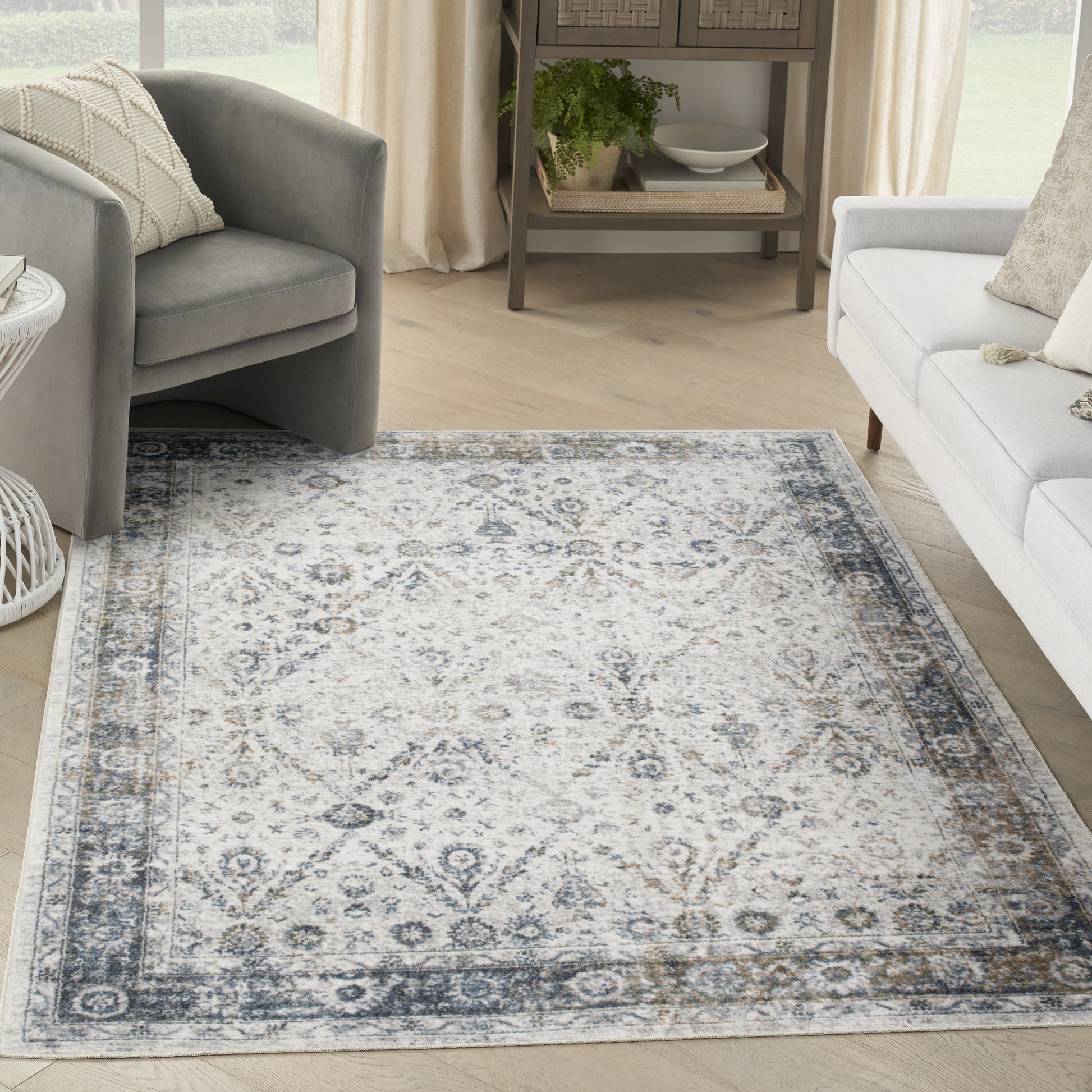 Cream area rug with blue-gray geometric medallion border in a modern living room with gray chairs.