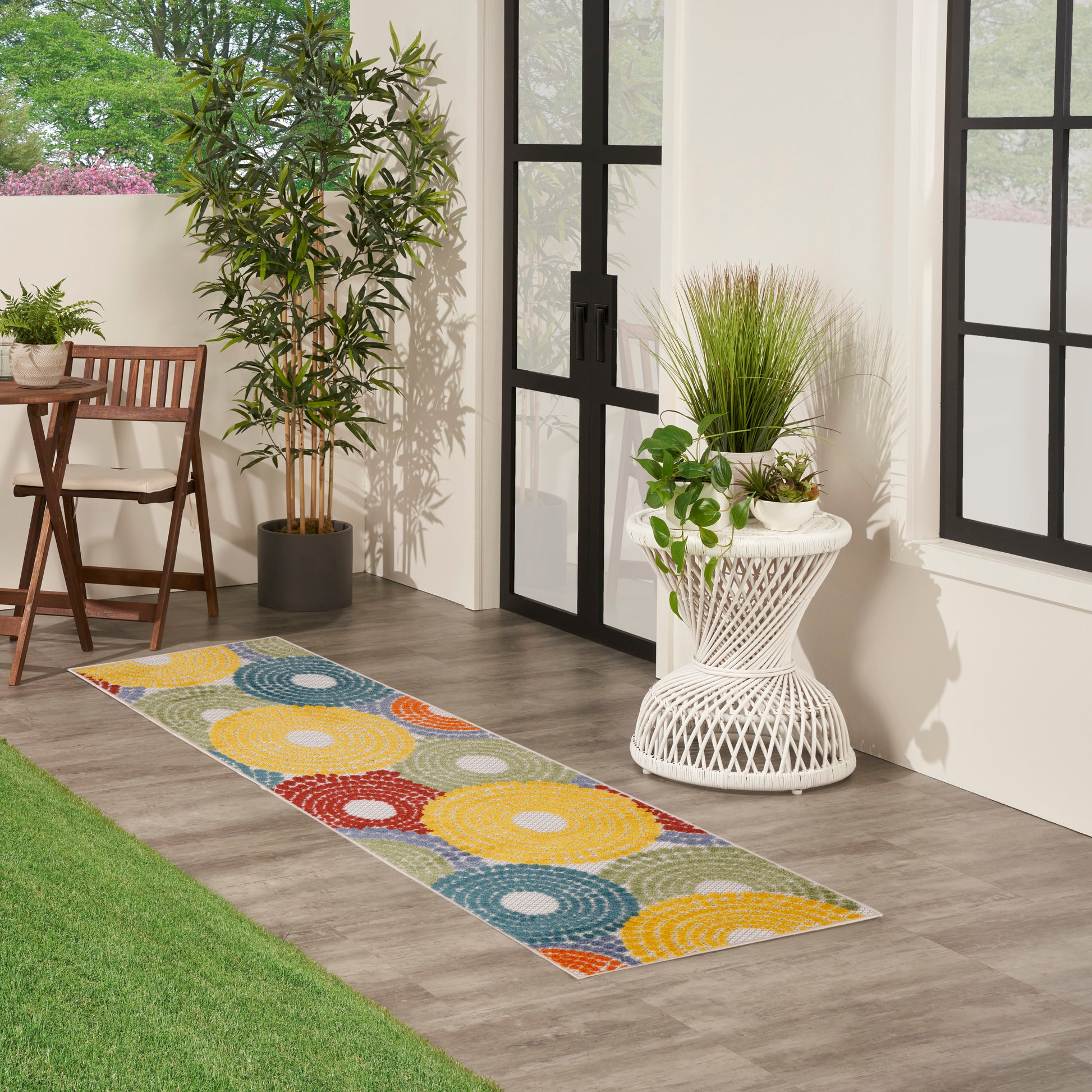 Multicolor circular-pattern runner rug on wood floor beside glass doors, with plants and wicker furniture.
