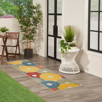 Multicolor circular-pattern runner rug on wood floor beside glass doors, with plants and wicker furniture.