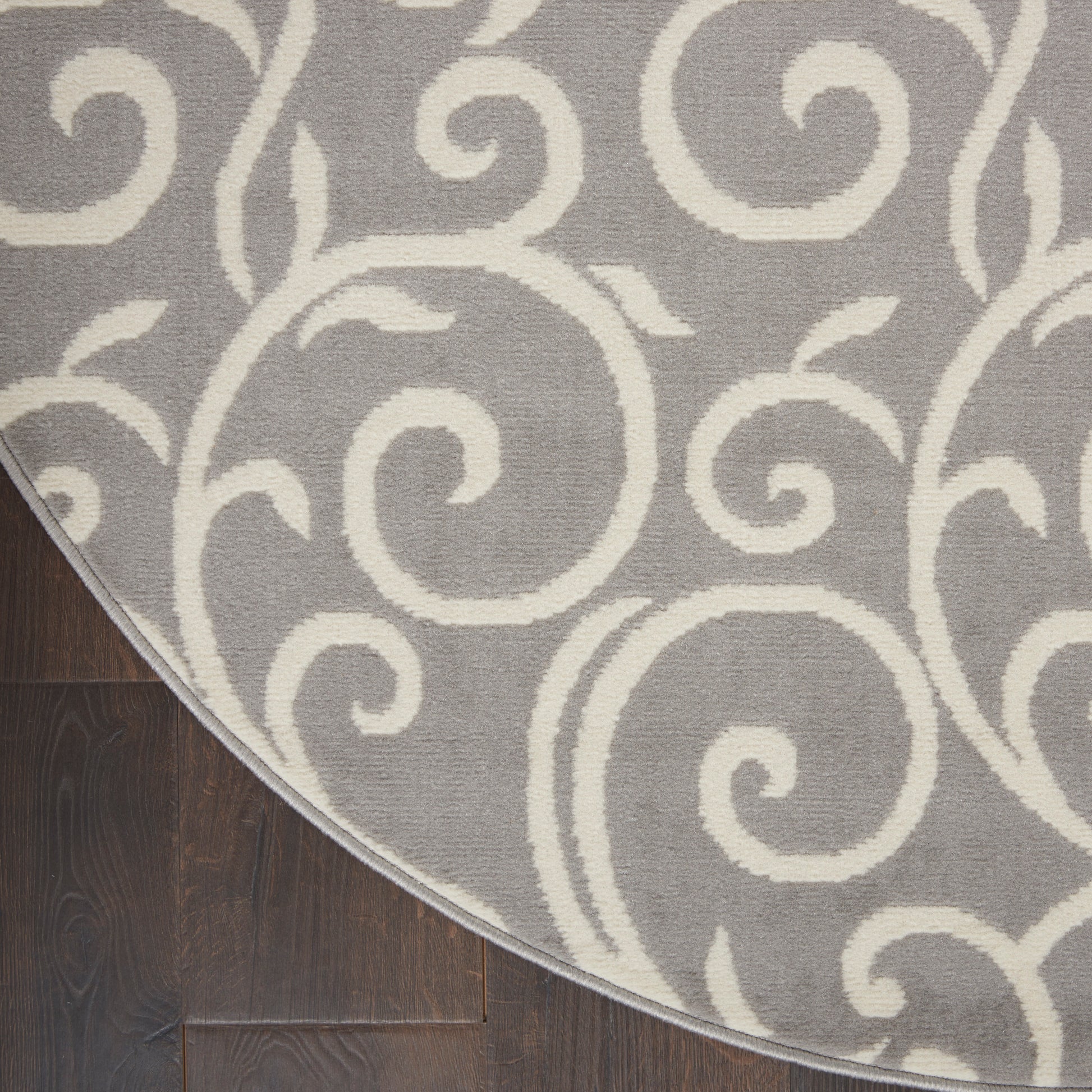 Round gray rug with ivory scrolling swirl pattern on dark wood floor; soft textured woven area rug.