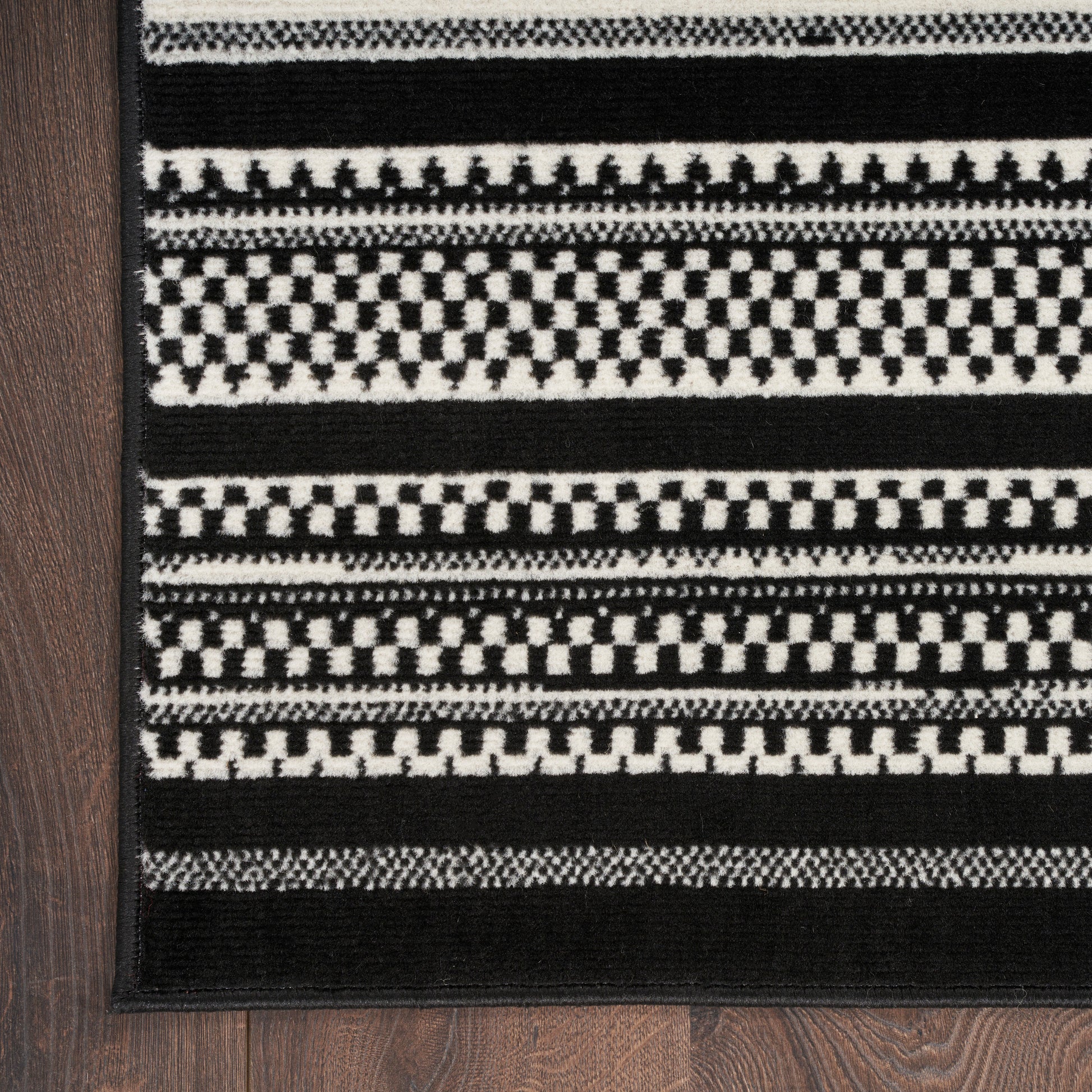 Black & white woven rug with alternating checkerboard & stripe patterns & dark border.