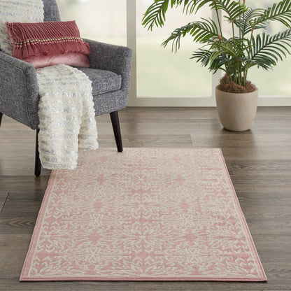 Pink patterned area rug on dark wood floor beside a grey armchair with a white throw and pink pillow, plant by the window.