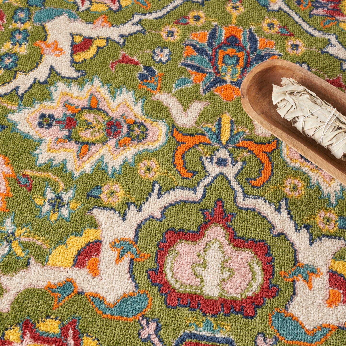 Colorful oriental rug with green base & multicolored floral motifs; wooden scoop holding sage bundles.