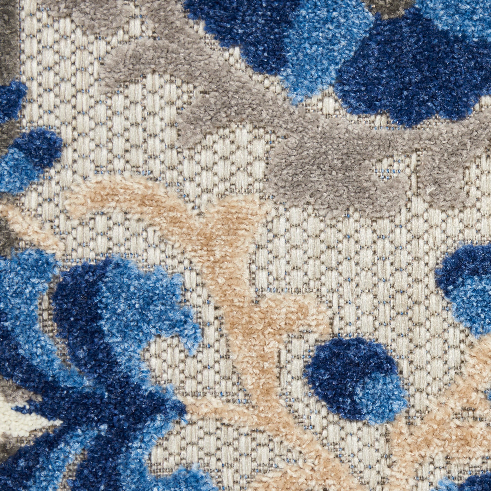Beige textured rug with blue floral motifs and tan vine accents on a woven backdrop.