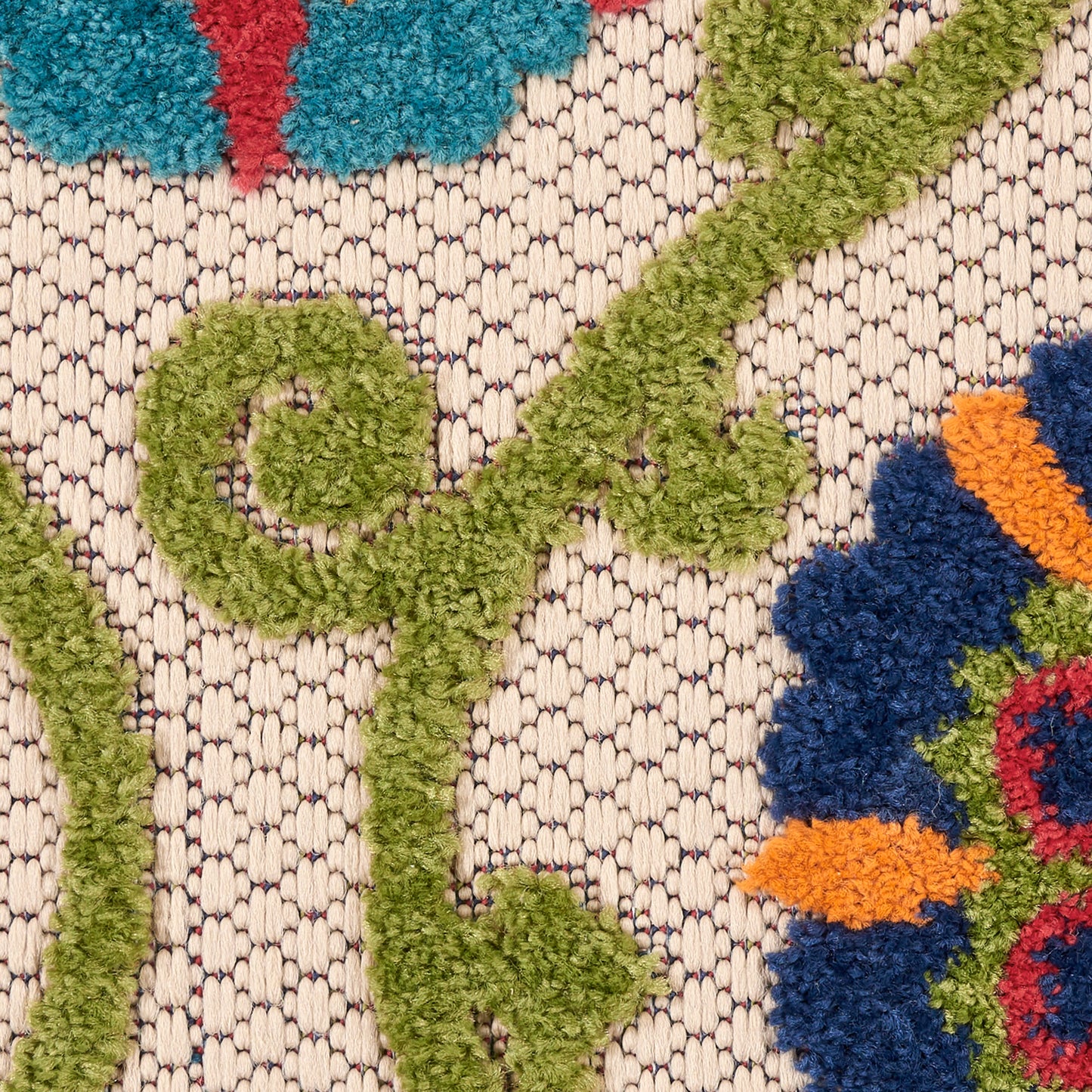 Close-up of a textured beige woven rug with lime green curling vines and bright blue, orange, and red floral accents.