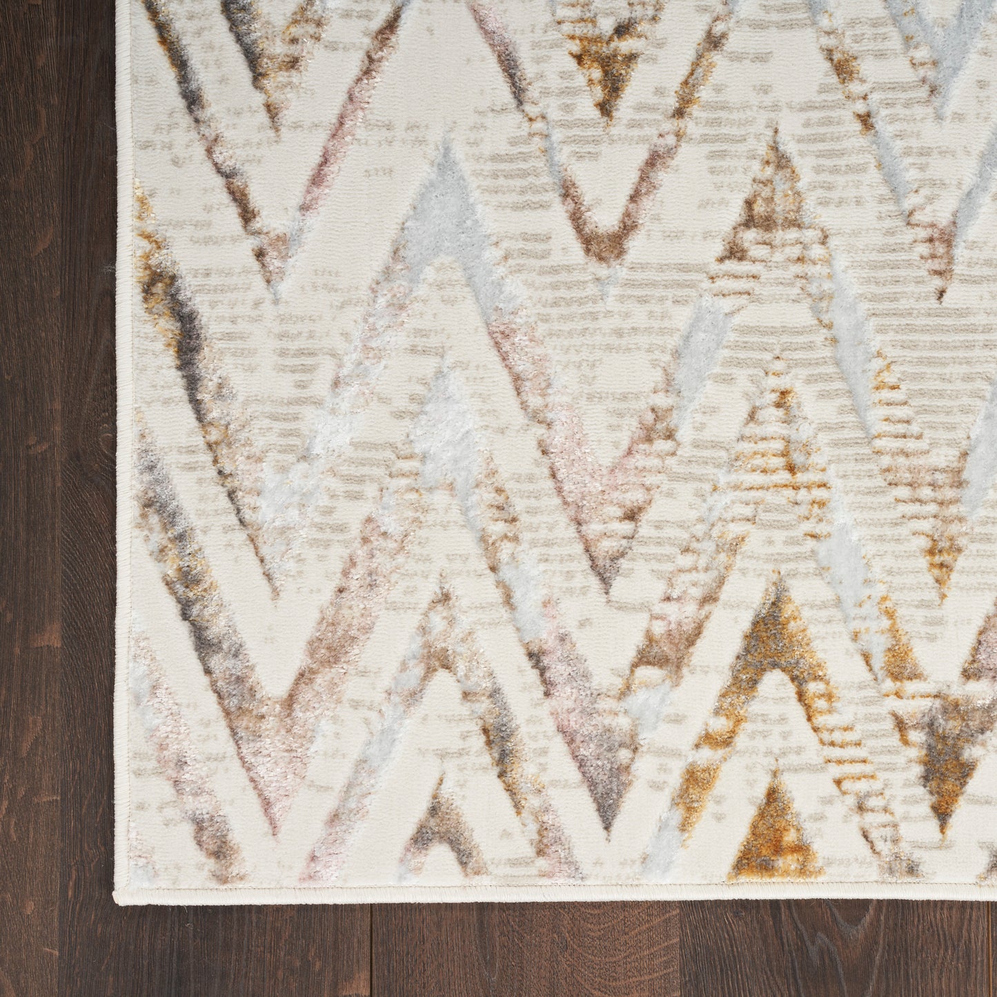 Chevron-pattern rug with cream base & pastel pink, gray & gold chevrons on dark wood floor; light border edge.