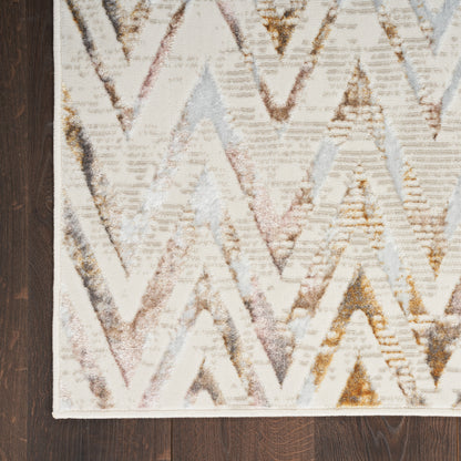 Chevron-pattern rug with cream base & pastel pink, gray & gold chevrons on dark wood floor; light border edge.