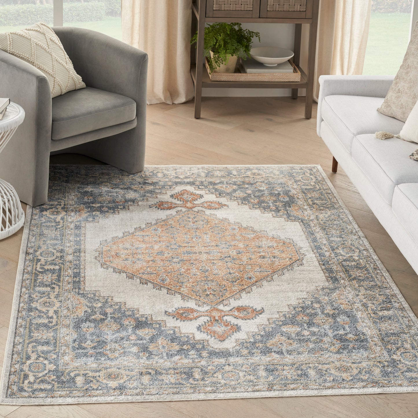 Rectangular soft-pile vintage-inspired rug with peach diamond medallion, blue-gray border, ivory background in bright living room.