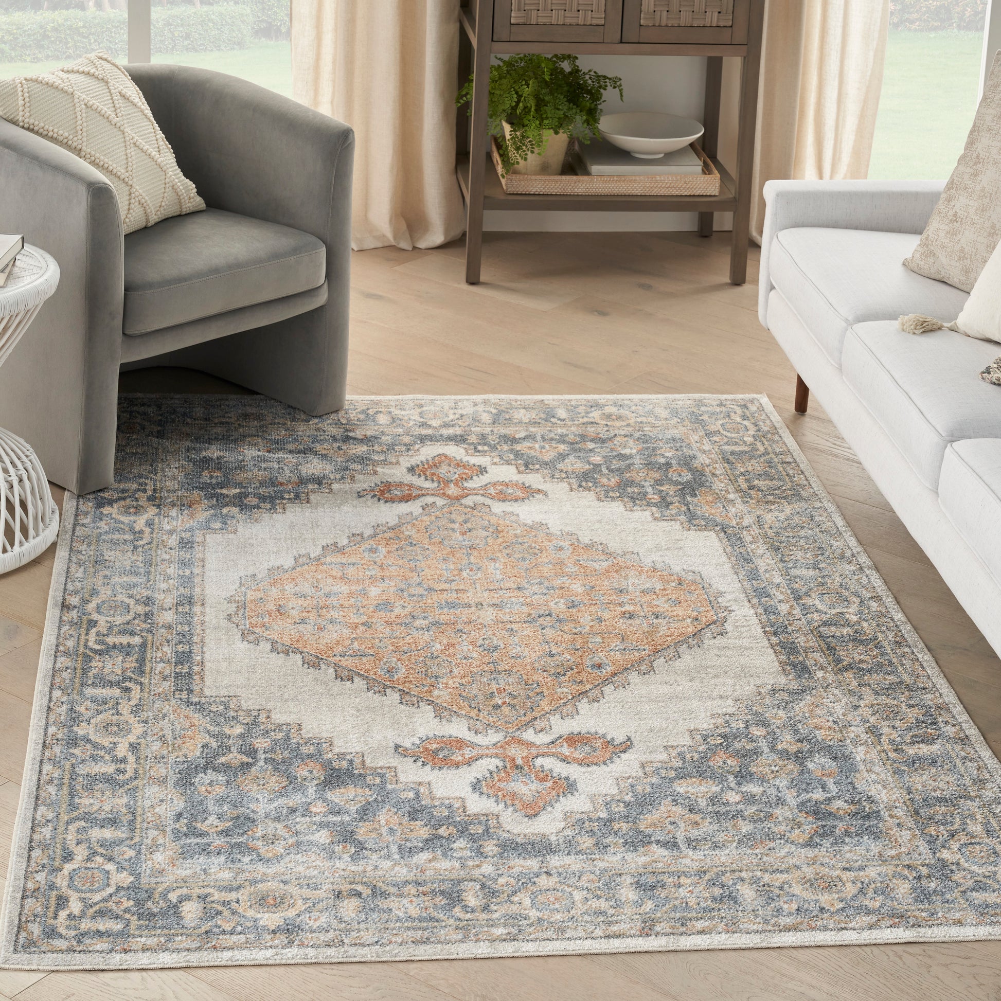 Rectangular soft-pile vintage-inspired rug with peach diamond medallion, blue-gray border, ivory background in bright living room.
