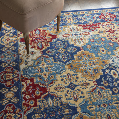 Ornate oriental-style area rug with blue, red, beige and gold floral medallion patterns under a beige upholstered chair.