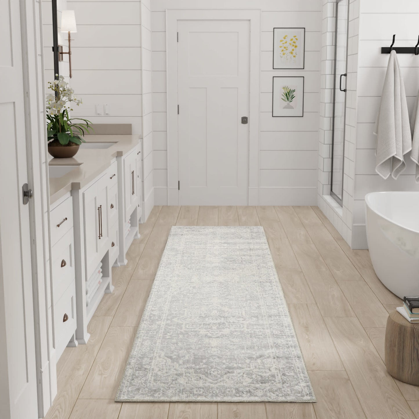 Light gray patterned bath rug runner on light wood floor in a white modern farmhouse bathroom with tub & glass shower.