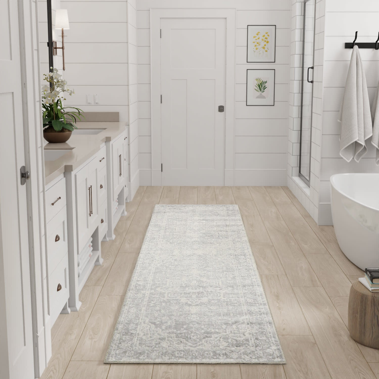 Light gray patterned bath rug runner on light wood floor in a white modern farmhouse bathroom with tub & glass shower.