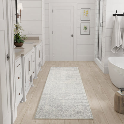 Light gray patterned bath rug runner on light wood floor in a white modern farmhouse bathroom with tub & glass shower.