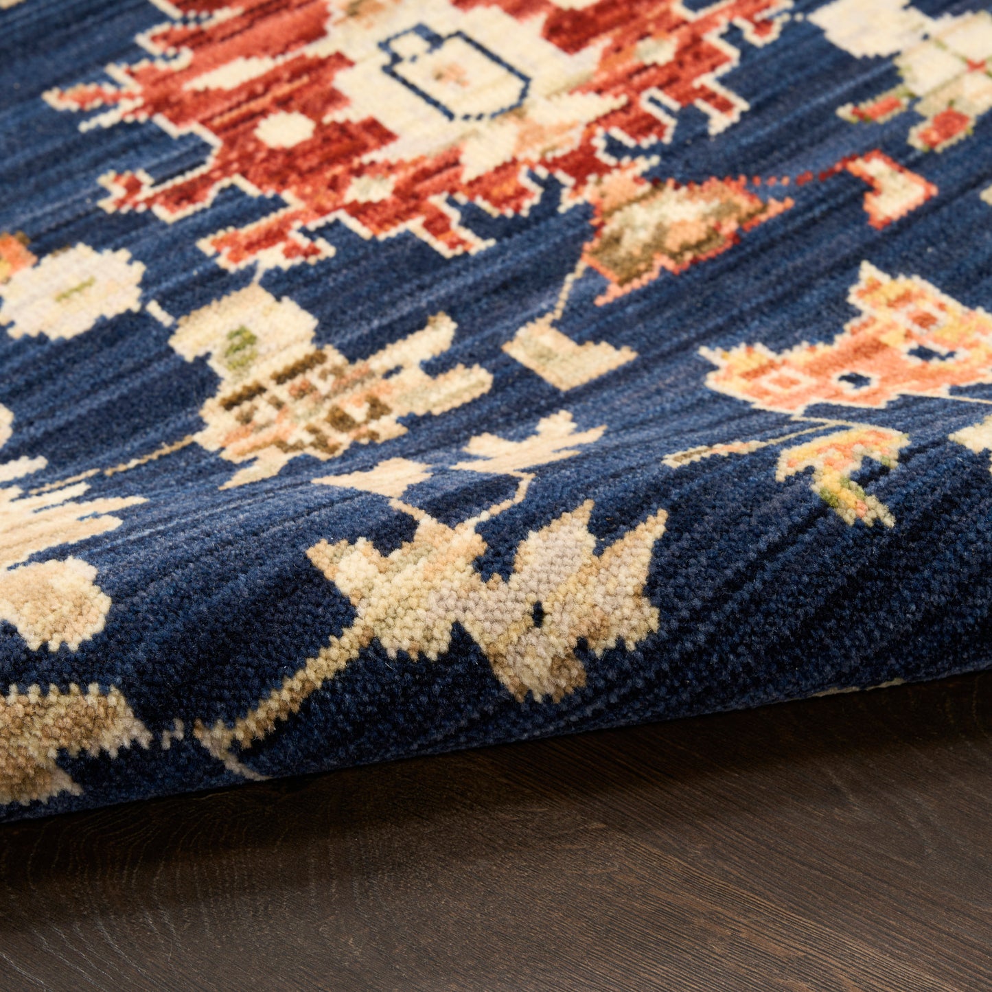 Close-up of navy blue rug with ivory floral motifs and red accents on dark wood floor.