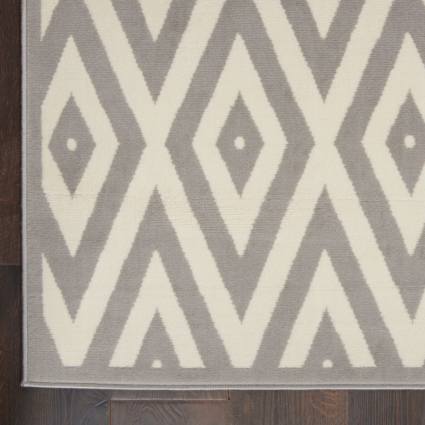 Gray and ivory diamond-pattern area rug on dark wood floor; modern geometric style.