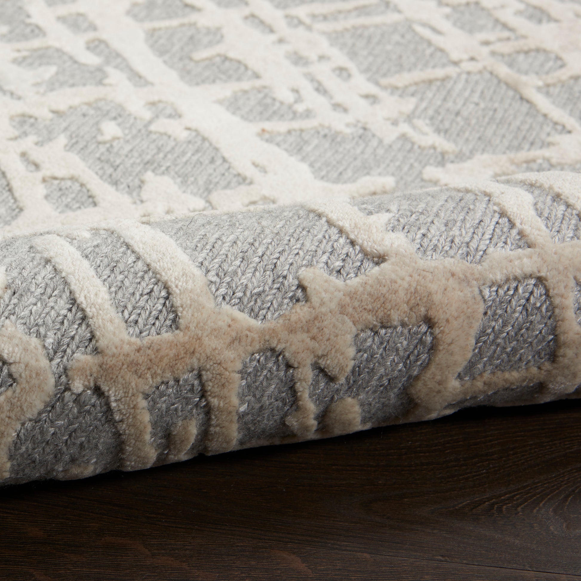 Gray and ivory geometric-pattern rug rolled at its edge on dark wood floor.