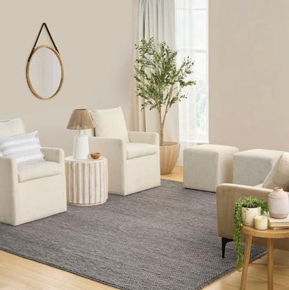Neutral living room with cream armchairs, gray rug, round wooden side table, potted plant, ottomans, and circular mirror.