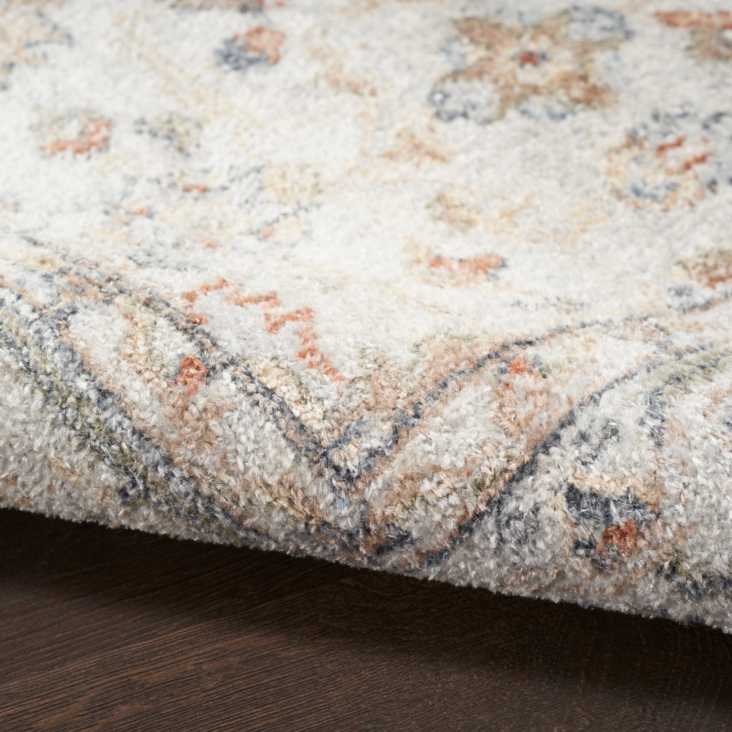 Cream tufted rug with blue-grey border and pale peach accents; soft plush pile on dark wood floor.