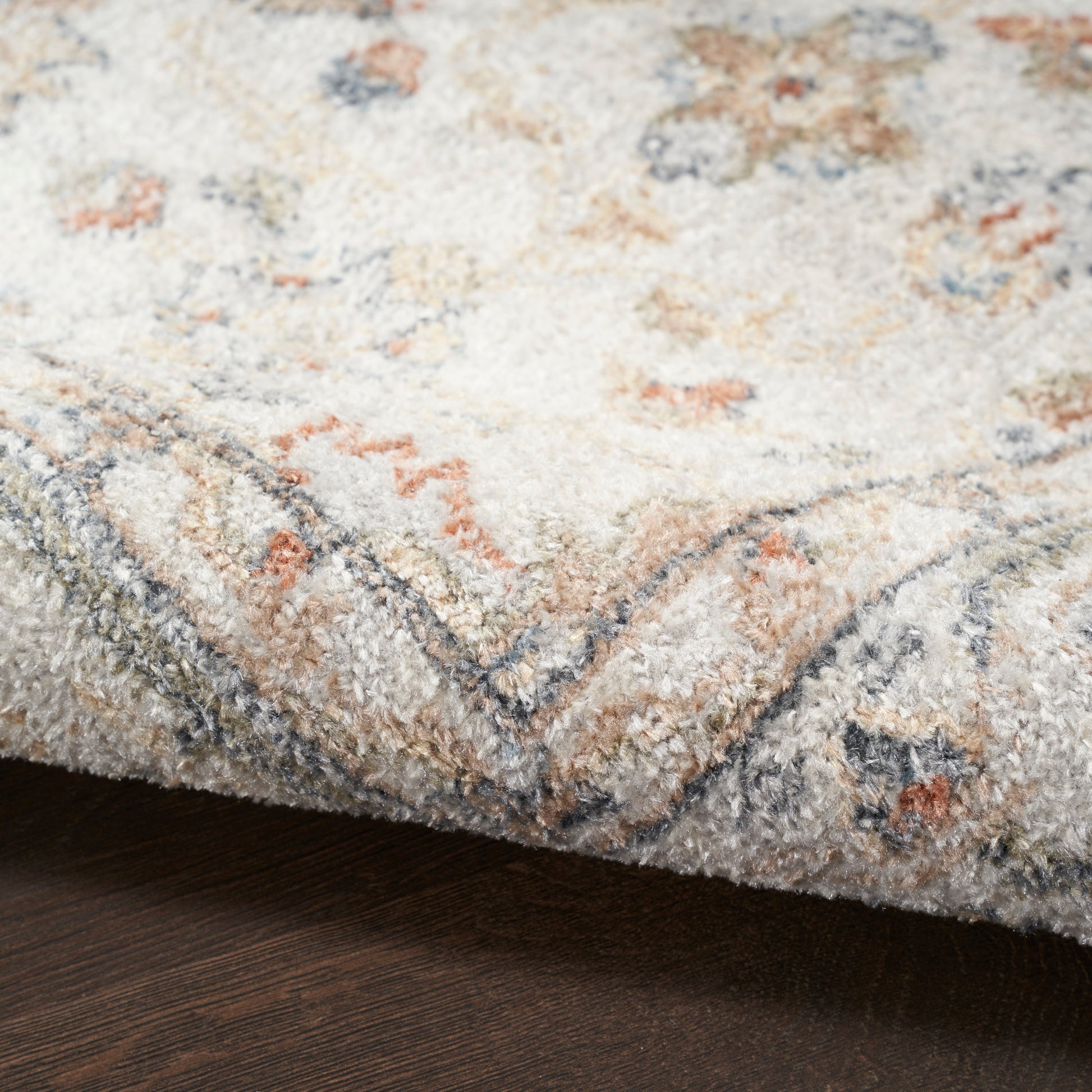 Cream tufted rug with blue-grey border and pale peach accents; soft plush pile on dark wood floor.