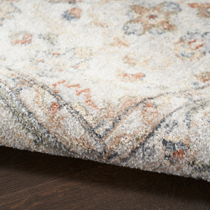Cream tufted rug with blue-grey border and pale peach accents; soft plush pile on dark wood floor.