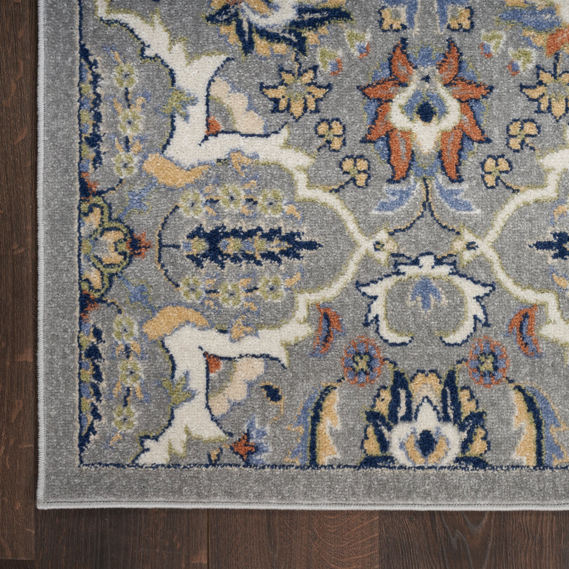 Gray ornate area rug with blue, gold, orange floral medallion pattern, bordered in lighter gray on dark wood floor.