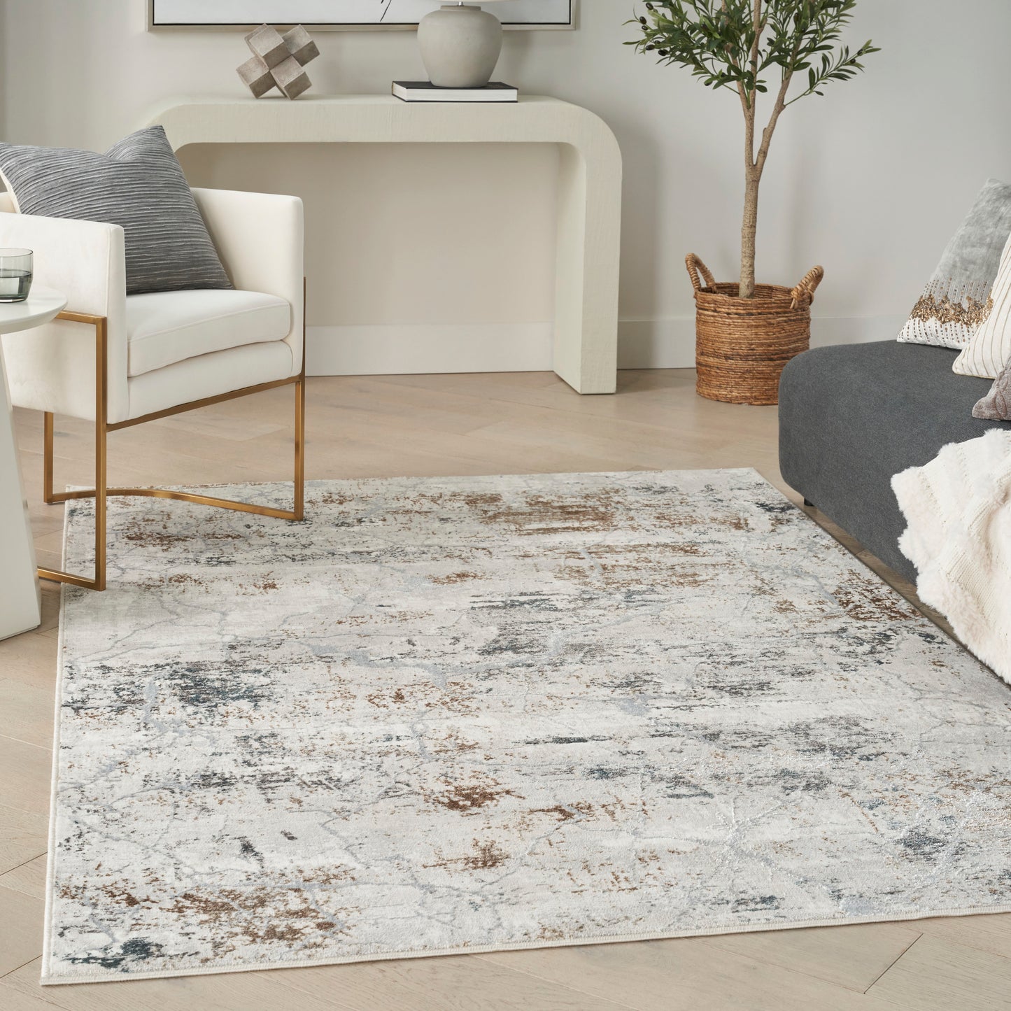 Living room with white chair on gold legs, distressed cream-gray rug, gray sofa, console table, plant in woven basket.