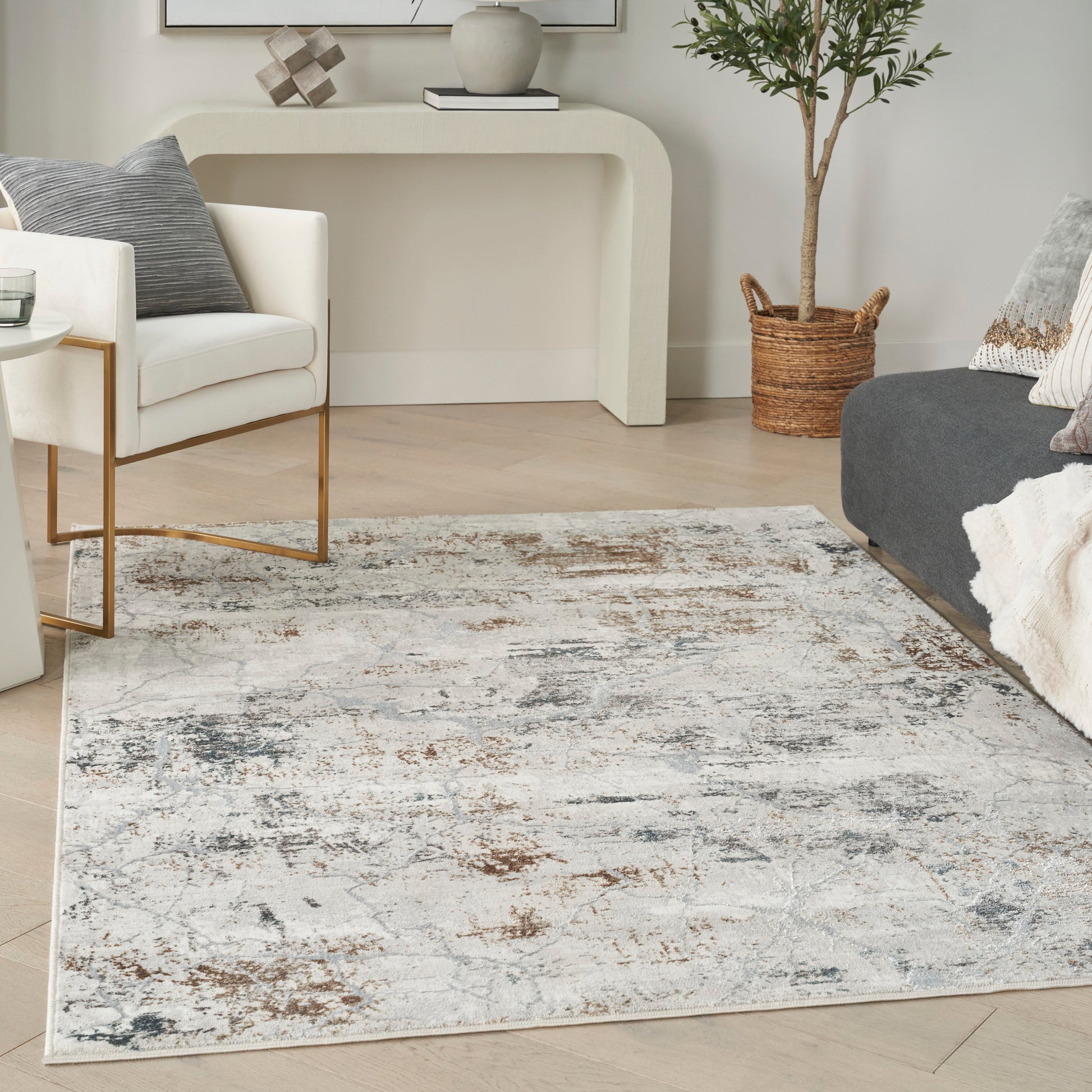 Living room with white chair on gold legs, distressed cream-gray rug, gray sofa, console table, plant in woven basket.