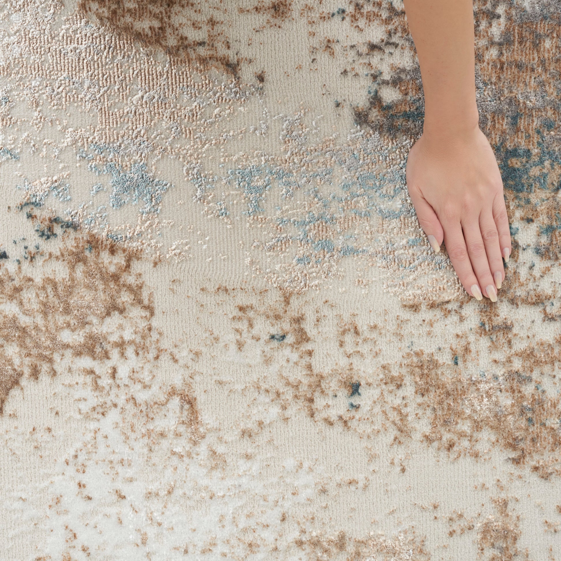 Beige and brown abstract area rug with blue accents; soft, textured pile; hand resting for scale.