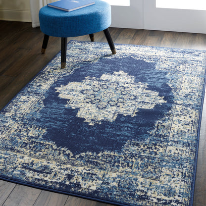 Distressed navy and ivory oriental rug with central medallion, paired with a round blue upholstered ottoman on wood floor.