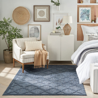 Neutral bedroom vignette: beige fabric armchair, blue patterned rug, white cabinet, wicker baskets, framed art, and bed.