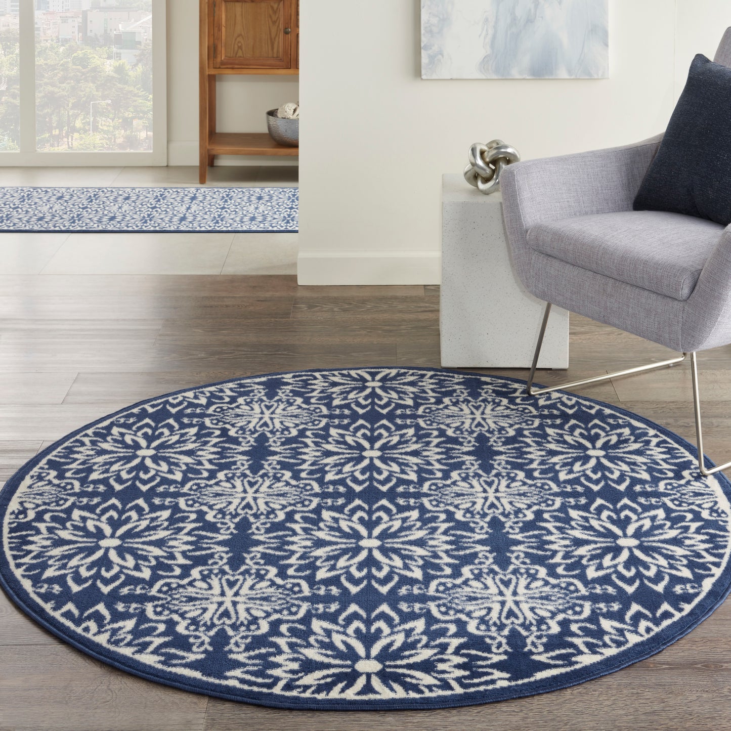 Round blue and white floral-patterned area rug on dark wood floor in a modern living room with a gray armchair.