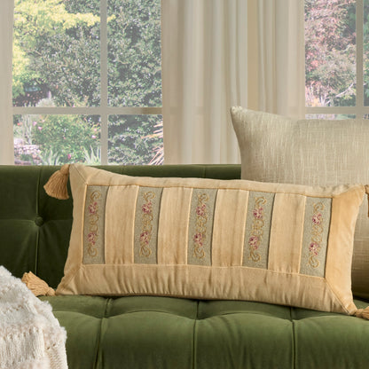 Beige rectangular decorative pillow with vertical floral-embroidered stripes and tassels on a green tufted sofa.