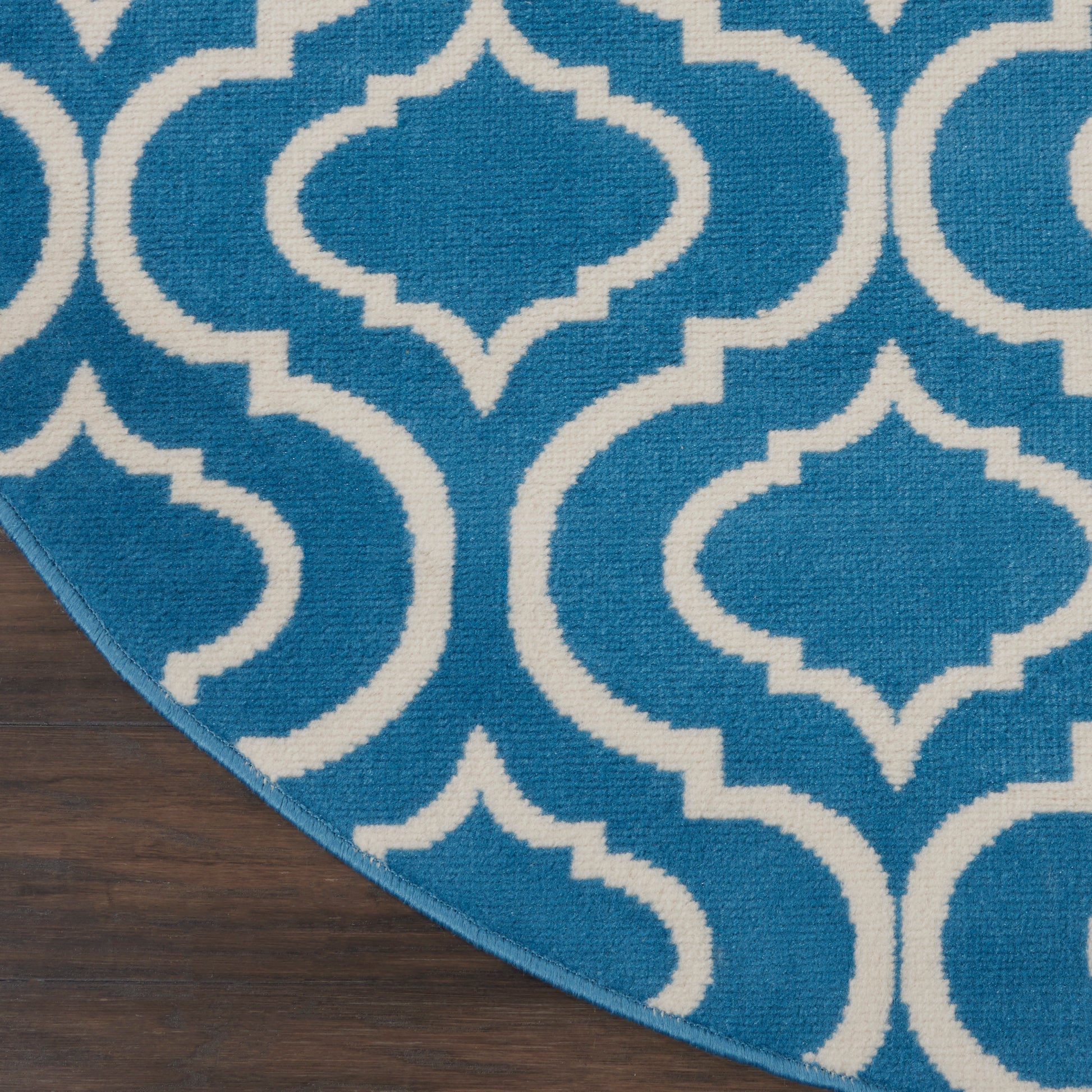 Blue rug with white Moroccan trellis pattern, interlocking curved shapes, on dark wood floor edge.