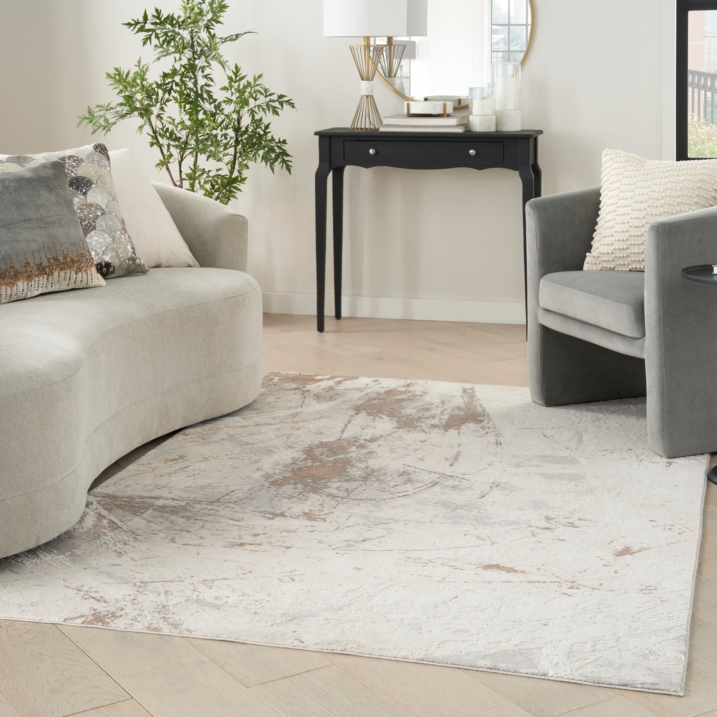 Neutral living room with beige curved sofa, gray armchair, beige-gray rug, black wood console table, plant and lamp.