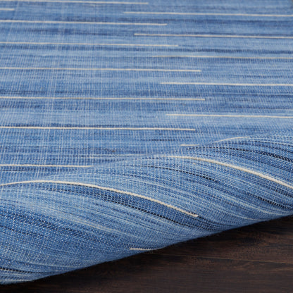 Blue woven rug with white horizontal stripes and a folded edge on a dark wood surface; 6' x 9'.