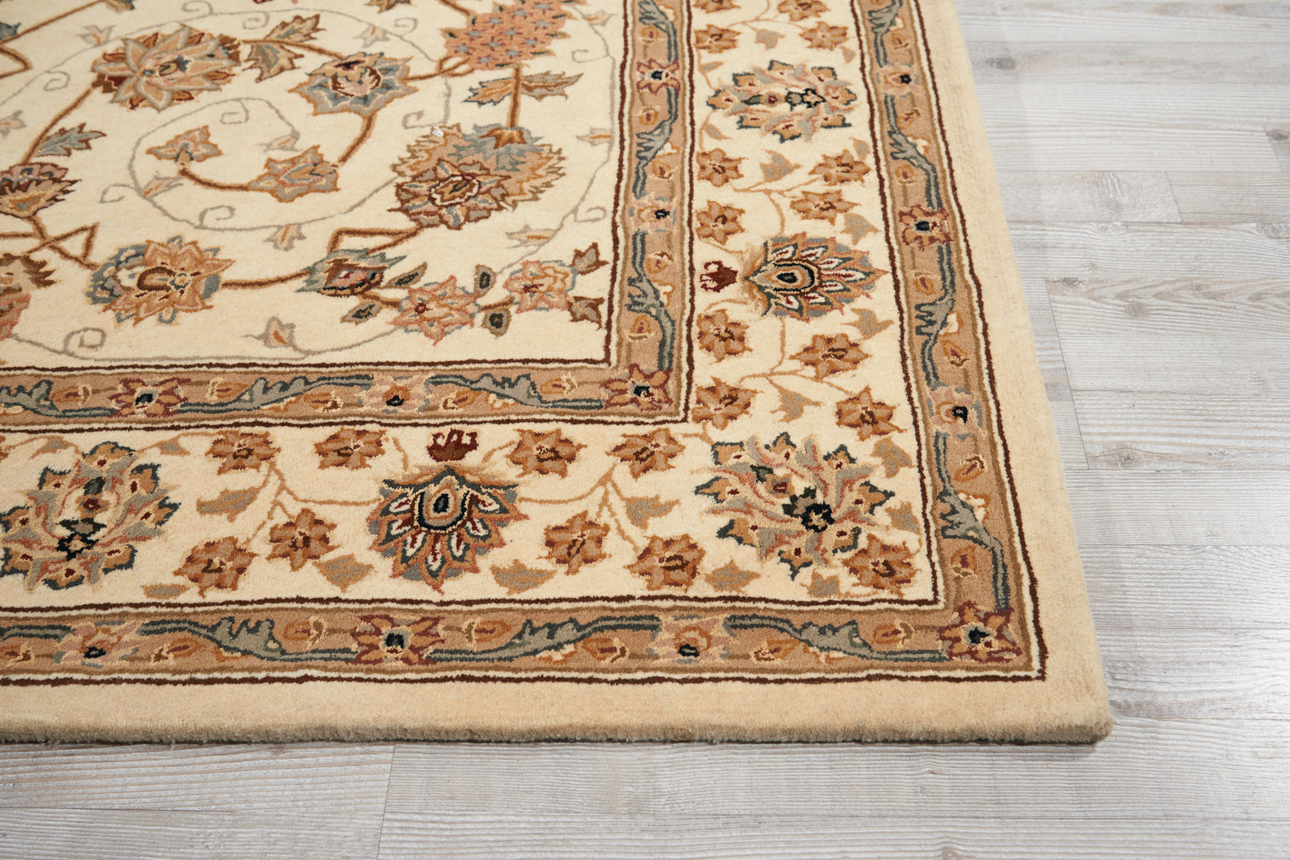Cream Persian-style area rug with blue and tan floral border and medallion motifs, fringed edge on light gray wood floor.