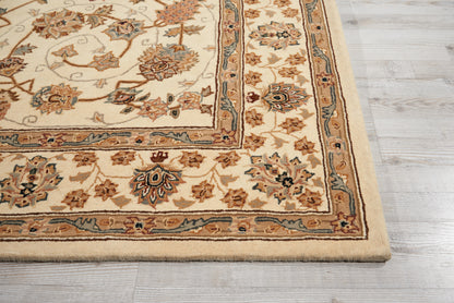 Cream Persian-style area rug with blue and tan floral border and medallion motifs, fringed edge on light gray wood floor.