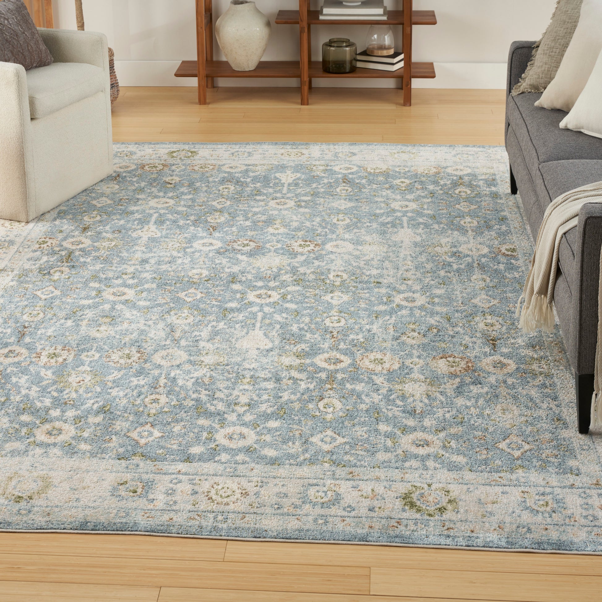 Blue and ivory distressed oriental-pattern area rug in a bright living room with light wood floor and gray sofa.