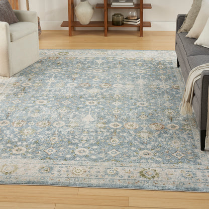 Blue and ivory distressed oriental-pattern area rug in a bright living room with light wood floor and gray sofa.