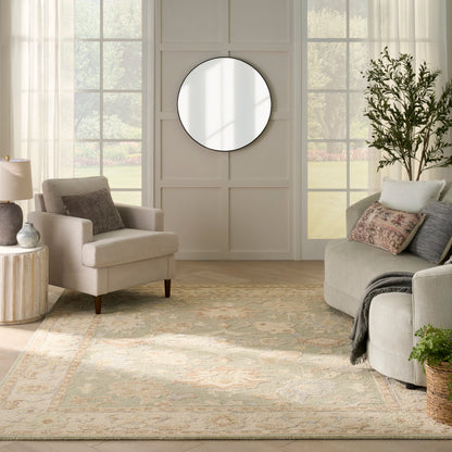 Neutral living room with beige chairs, a round wall mirror, patterned light rug, plant, and cozy textiles.