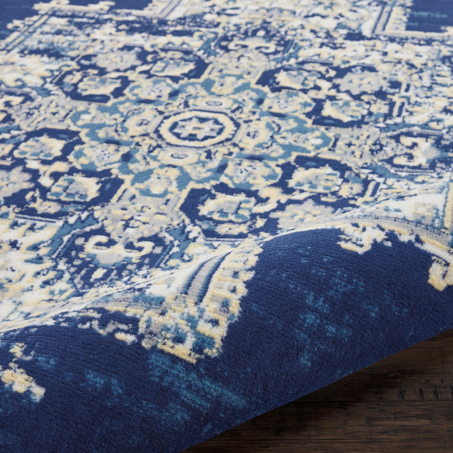 Blue oriental round rug with cream and pale blue intricate medallion pattern; rolled corner on wooden floor.