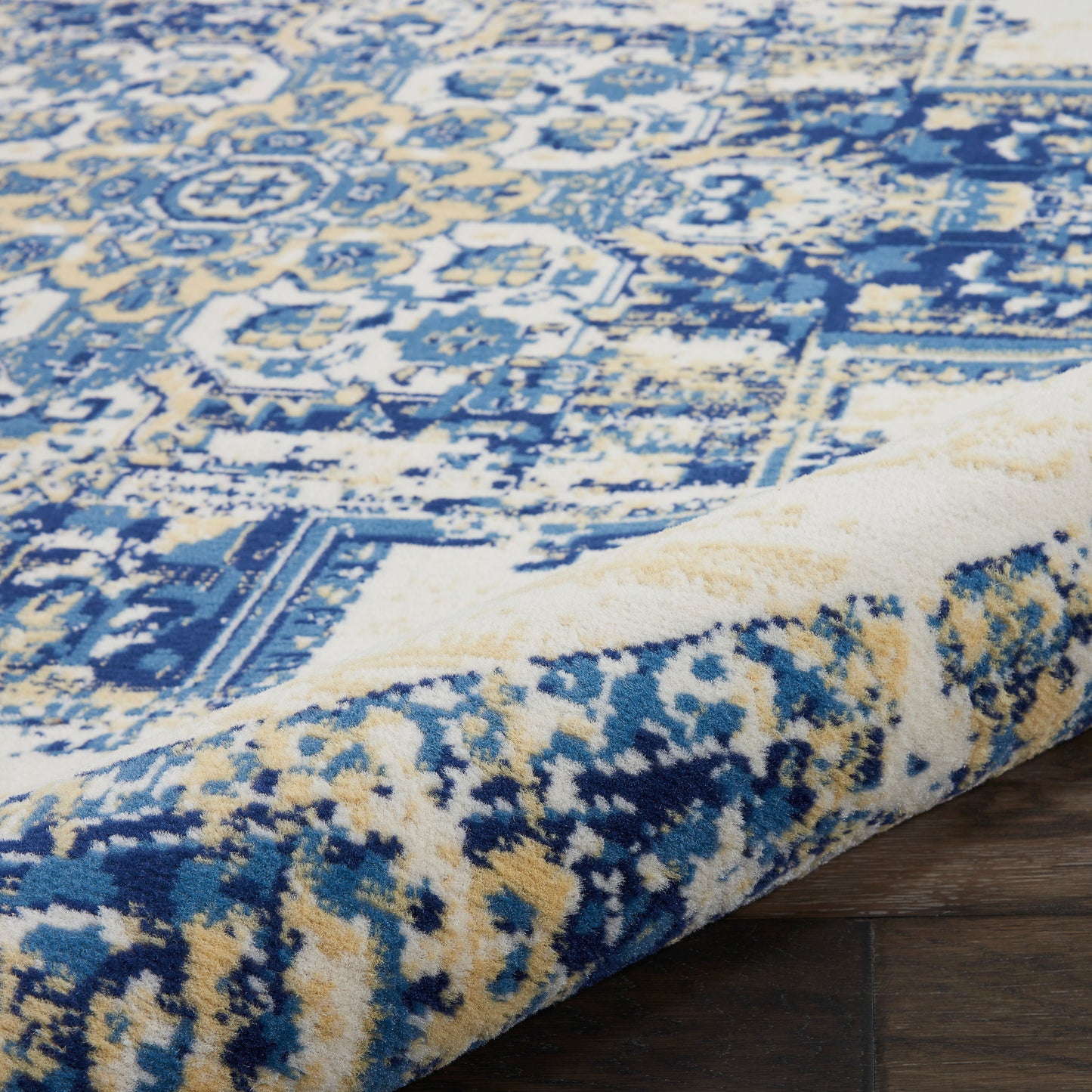 Blue and cream geometric area rug with a distressed antique pattern, rolled at the edge on wooden floor.