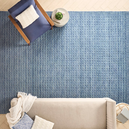 Overhead view: blue textured rug, beige sofa with cream throw, navy wood-armchair with white cushion, small round table with plant