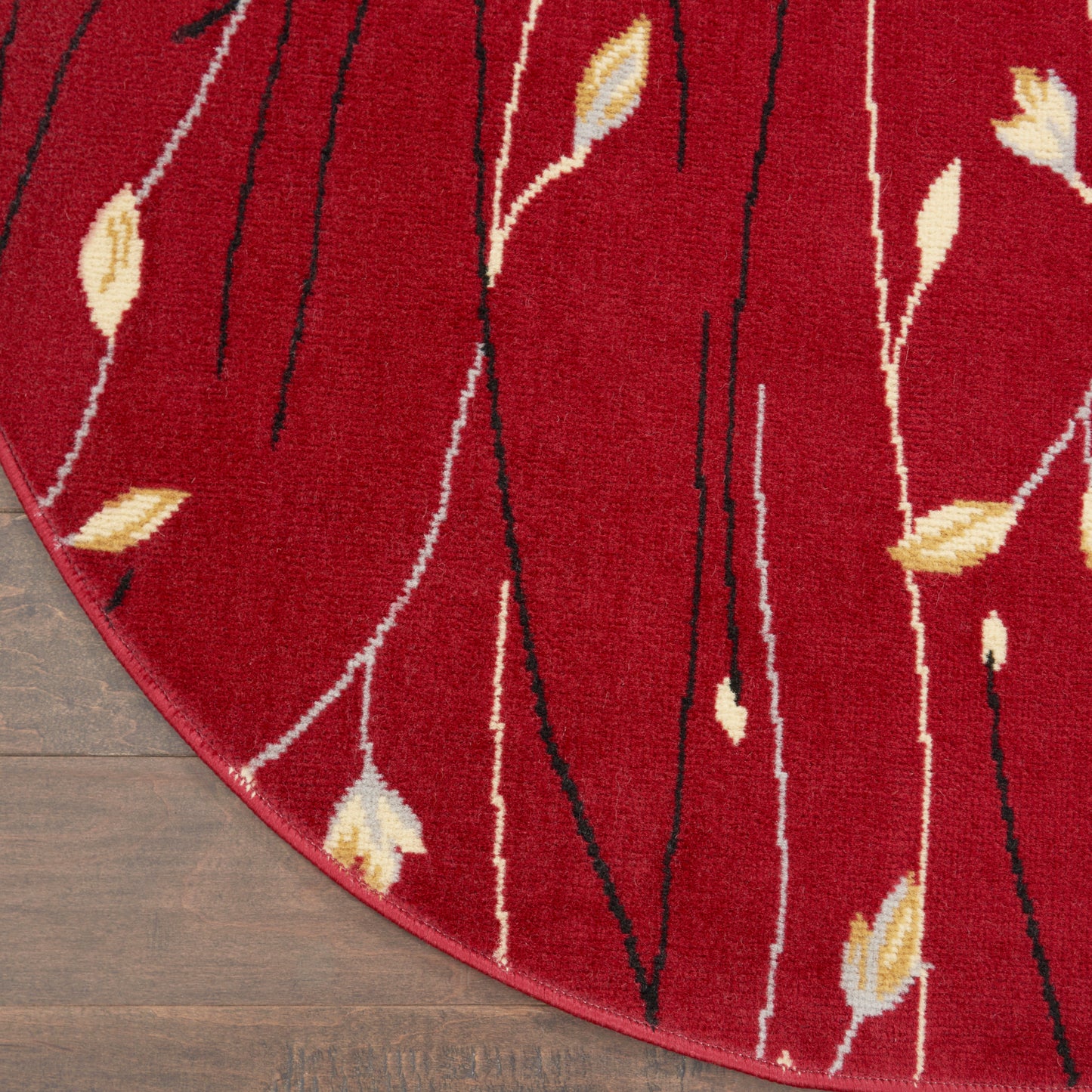 Red circular rug with cream and yellow leaf motifs and slender black and white stems on a wooden floor.